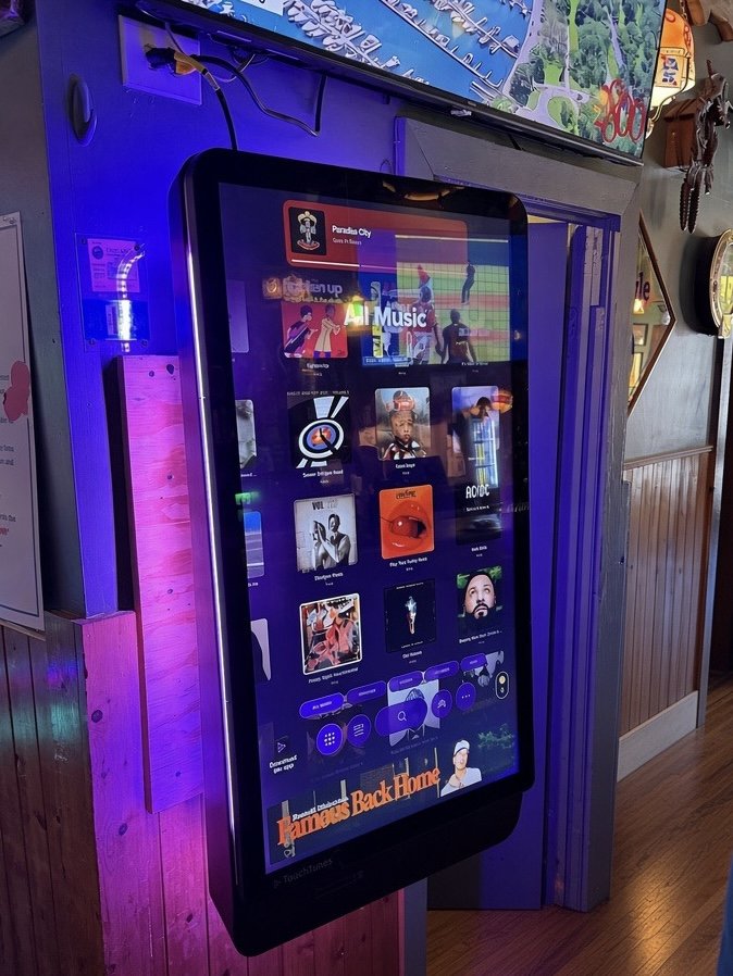 TouchTunes Soundwave jukebox mounted on a bar wall, glowing purple and blue
