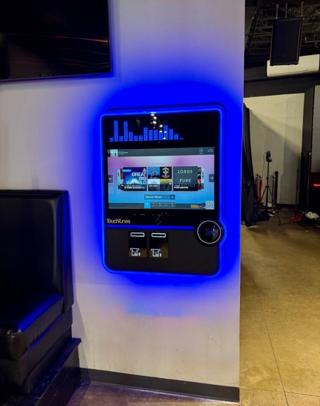 Wall-mounted TouchTunes jukebox glowing blue at The Landing in Starkville, Mississippi
